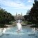 Un gran edificio adornado con vista a una gran fuente circular, varias jardineras y dos fuentes